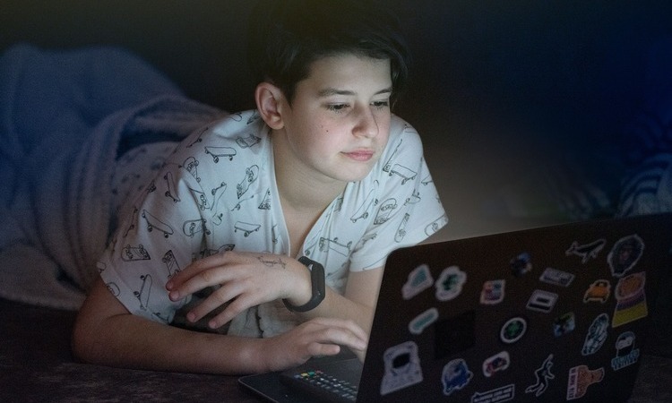 Teenager using a laptop covered in stickers at night.
