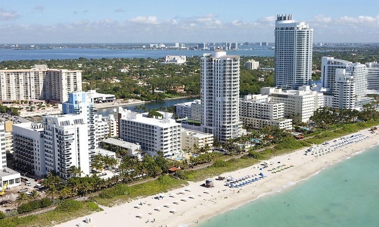 Aerial view of Miami Beach's high-rise condominiums and hotels lining the shoreline, with the ocean and coastal waterways in the background.