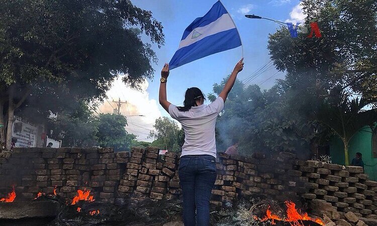 Woman waving Nicaragua's flag near a burning barricade during 2018 anti-government protests.
